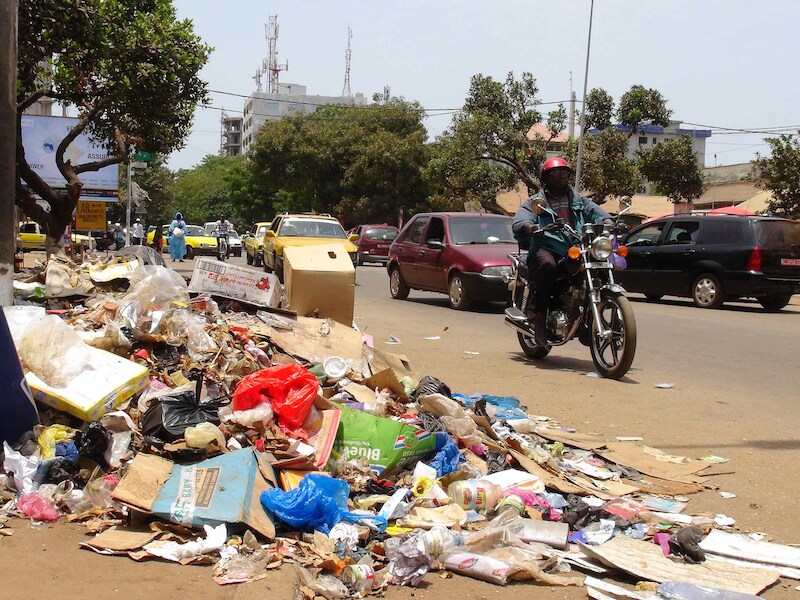 Een motorrijder passeert een berg afval in de hoofdstad Conakry.