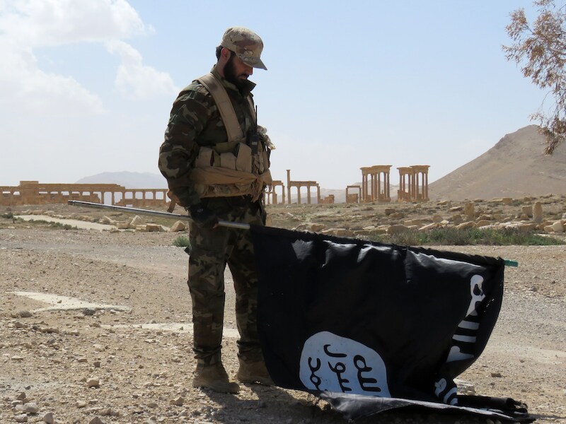 Een Syrische soldaat houdt een IS-vlag vast na de herovering van de stad.