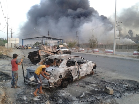 Kinderen staan naast een uitgebrande auto in Mosul, de noordelijke Iraakse stad die in handen is gevallen van ISIS.