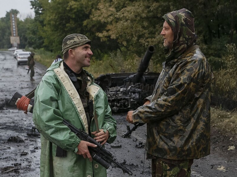 Oekraïense militairen naast een verwoeste tank van de rebellen.
