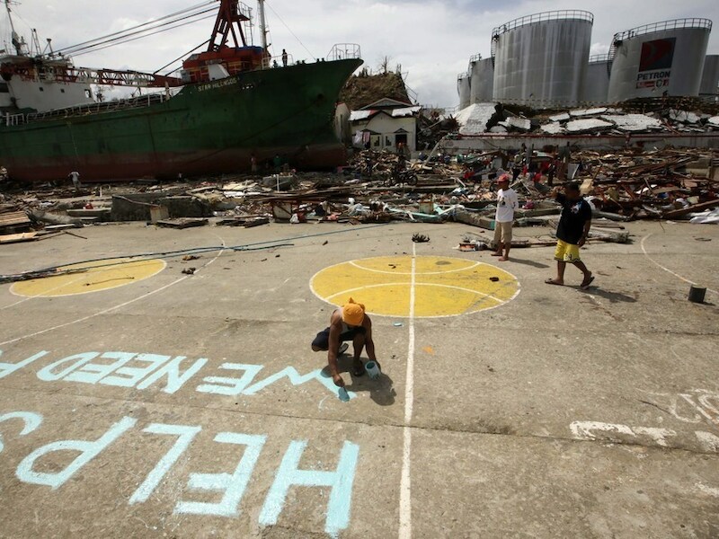 Een Filipijnse vrouw schildert een oproep voor help op straat in het zwaargehavende Tacloban.