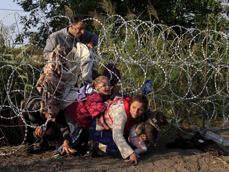Syrische migranten kruipen onder een hek aan de Hongaars-Servische grens.