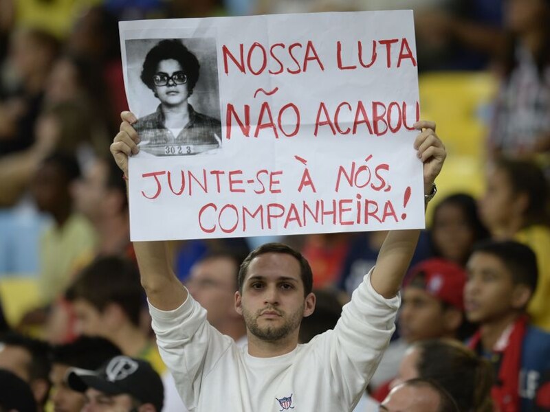 Een betoger houdt een poster in de lucht met de foto van president Dilma Rousseff met als tekst "De strijd is niet over. Vervoeg ons, vriendin".