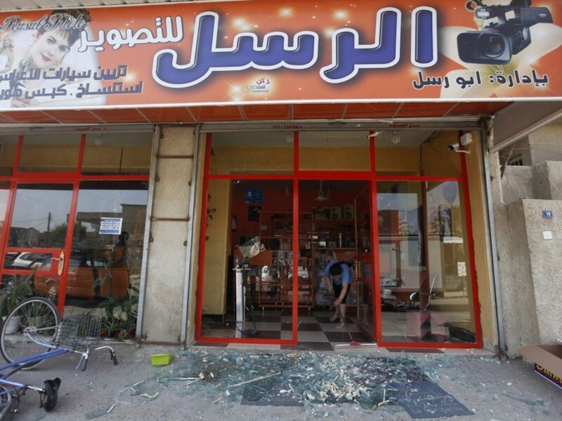 Een winkelier in Bagdad veegt glasscherven op, nadat de winkelruit bij de bomaanslag is gesneuveld.