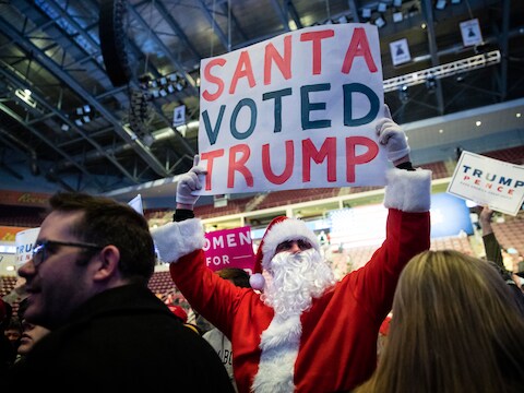Een man met een kerstmanpak houdt een bord omhoog waarop staat dat 'de Kerstman voor Trump heeft gestemd'.