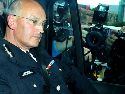 Paul Stephenson verlaat na de zitting het Britse parlement. Persfotografen belegeren de wagen.