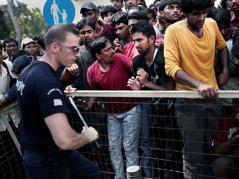 Een politieagent op Kos probeert maandag een grote groep vluchtelingen in bedwang te houden die zich bij een politiebureau willen laten registeren.