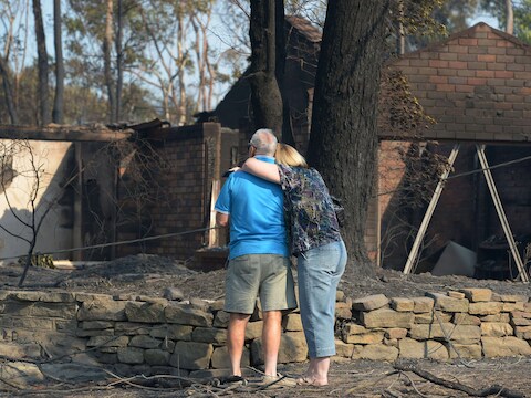 Een echtpaar aanschouwt de resten van zijn uitgebrande woning in Winmalee, in de Blue Mountains ten westen van Sydney.