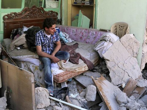 Een Syrische man in de puinhopen vam een slaapkamer nadat een vatenbom op het huis is gevallen.