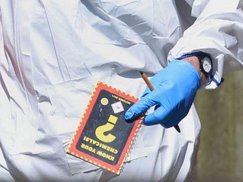 Een speurder verlaat de woning van de dader met het handboek 'Ken je chemische stoffen'.