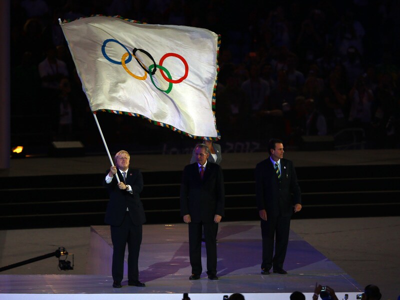 Boris Johnson zwaait vier keer met de olympische vlag alvorens die door te geven.