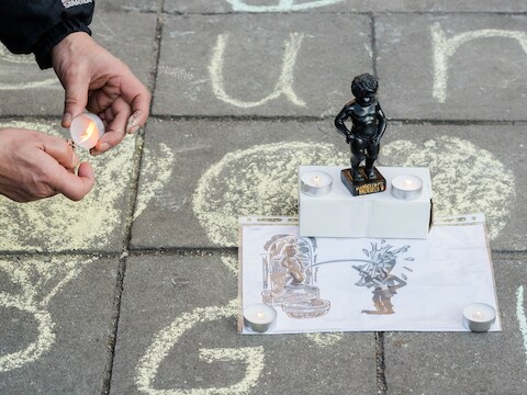 Een man ontsteekt een kaars naast een beeldje van Manneken Pis op het Beursplein in Brussel, de dag van de aanslagen.
