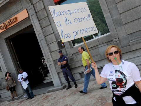 Aan het hoofdkwartier van de Liberbank in Oviedo werd vandaag geprotesteerd. Een ontevreden vrouw houdt een bord omhoog waarop staat: "Bankiers als eerste naar de gevangenis!"