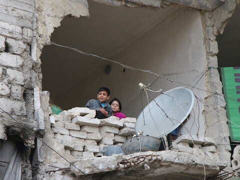 Kinderen kijken naar buiten in een huis dat zwaar geleden heeft onder het oorlogsgeschut in Aleppo.