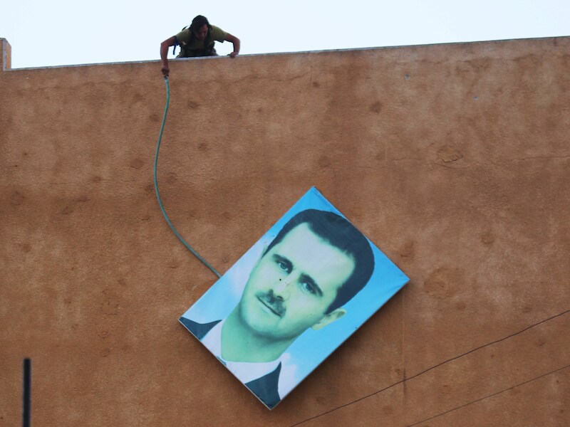 Een lid van de aan al-Qaida gelieerde rebellengroep al-Nusra verwijdert in de Syrische stad Ariha een portret van president Bashar al-Assad.