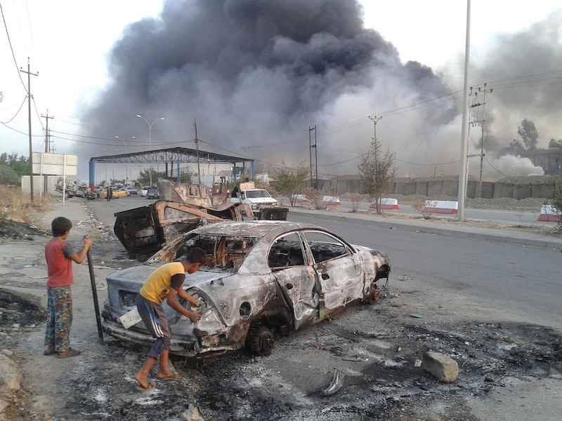 Kinderen staan naast een uitgebrande auto in Mosul, de noordelijke Iraakse stad die in handen is gevallen van ISIS.