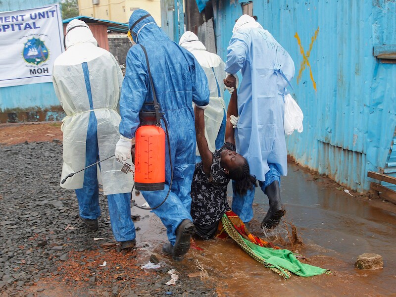 Een vrouw die vermoedelijk lijdt aan het ebolavirus wordt door gezondheidsmedewerkers naar een behandelcentrum in Liberia gebracht.