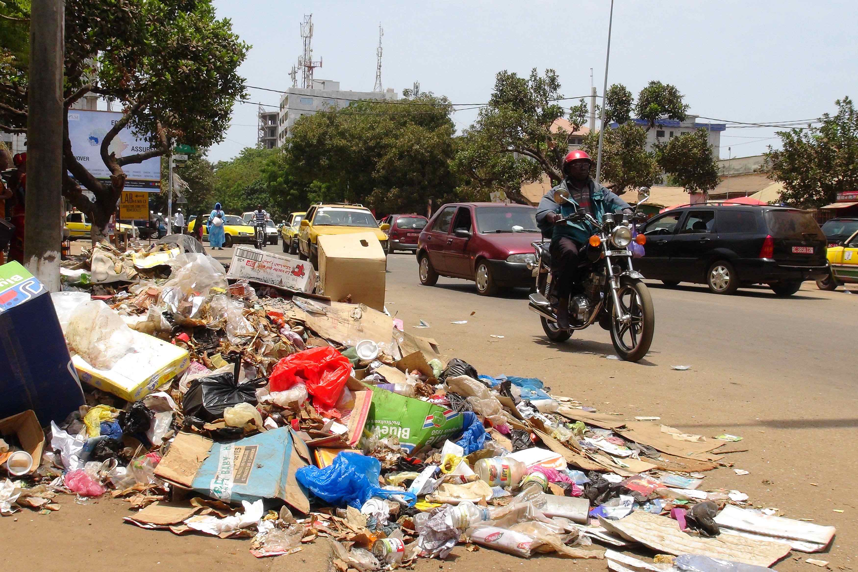 Een motorrijder passeert een berg afval in de hoofdstad Conakry.