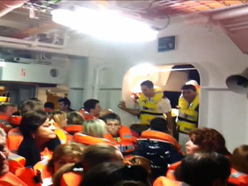 Crewelden in reddingsvesten begeleiden passagiers op een reddingsboot. Andere bemanningsleden kweten zich minder plichtsbewust van hun taak.