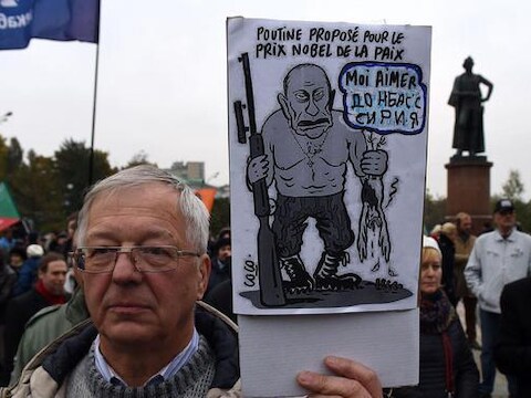 Een man tijdens de demonstratie van zaterdag in Moskou. Hij houdt een bord omhoog met daarop een spotprent van Poetin: 'Poetin voorgedragen voor de Nobelprijs voor de vrede, Ik hou van Donbass en Syrië'