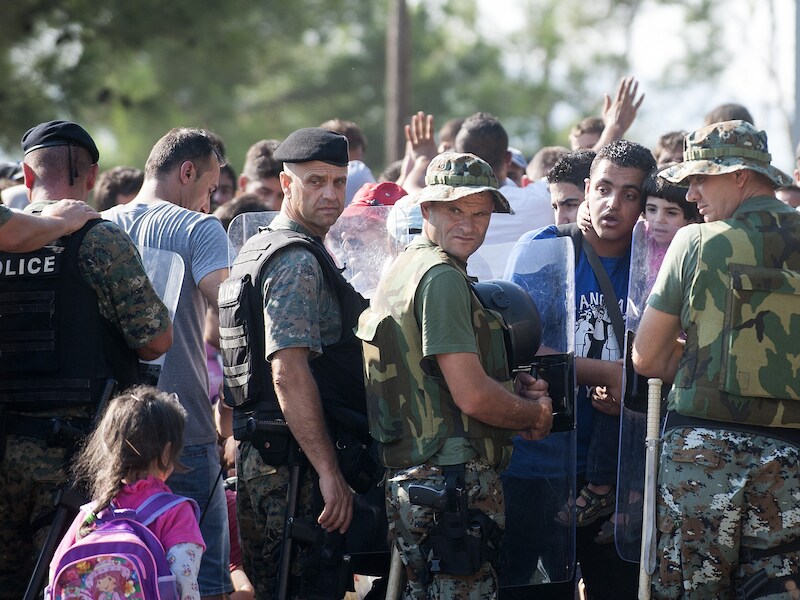 Migranten wachten bij een rij agenten aan de Macedonische grens.