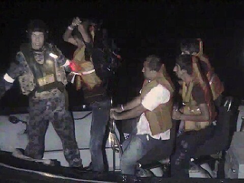 Leden van de Australische marine begeleiden asielzoekers naar een Indonesisch schip.