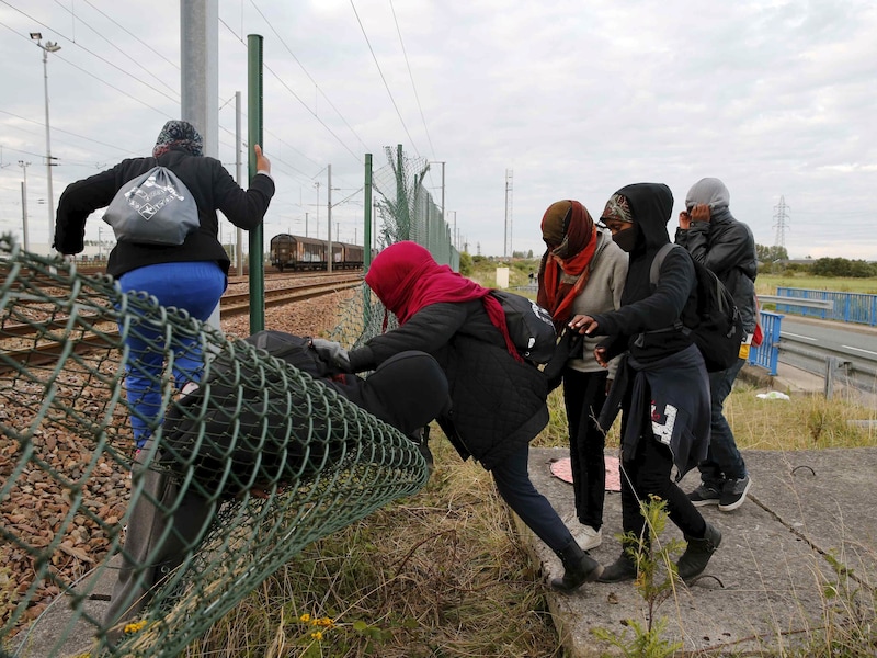 Vluchtelingen klimmen in Calais over een hek om de spoortunnel van de Kanaaltunnel te bereiken.
