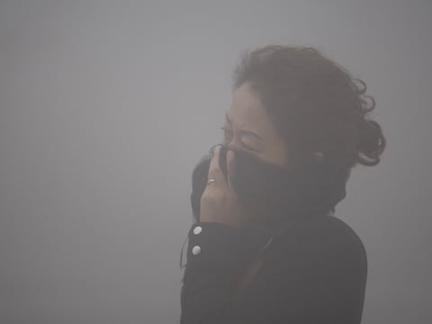 Een Chinese vrouw bedekt op dit archiefbeeld van 21 oktober 2013, haar mond tegen de smog in haar stad Harbin.
