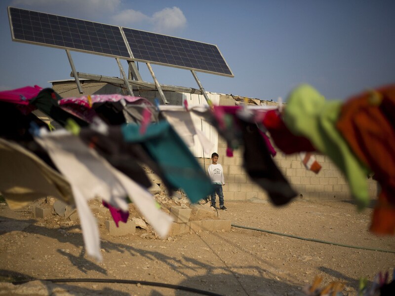 Een Bedoeïne jongen staat onder zonnepanelen die voor elektriciteit in zijn dorp in de Negev-woestijn zorgen.
