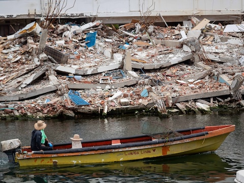 Iemand passeert met de boot voorbij een ingestorte woning.