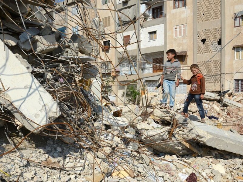 Kinderen poseren bij een vernield huis in Aleppo.