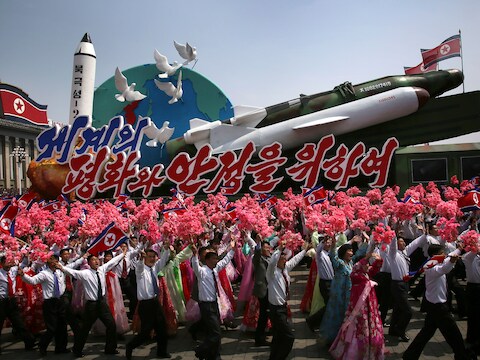 Noord-Koreanen zwaaien met de vlag van het land en plastic bloemen terwijl een vloot met raketten en het opschrift 'Voor vrede en stabiliteit in de wereld' voorbijkomt tijdens de militaire parade ter ere van de 'Dag van de Zon'.