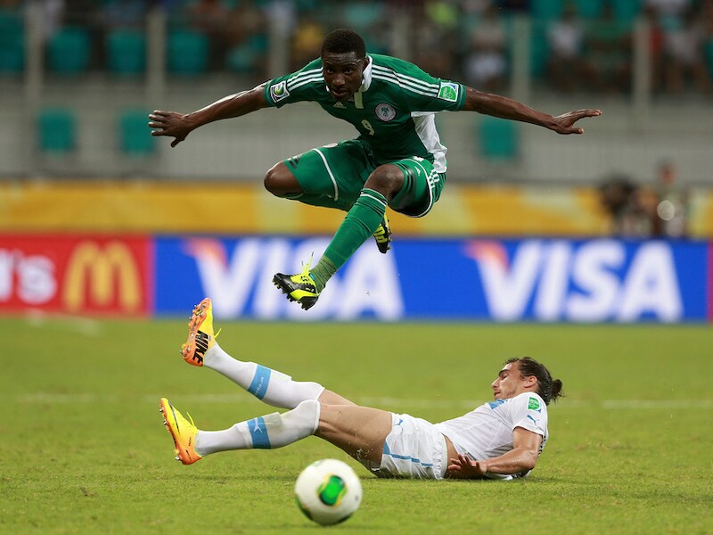 Joseph Akpala van Nigeria springt over de tackle van Martin Caceres van Uruguay.