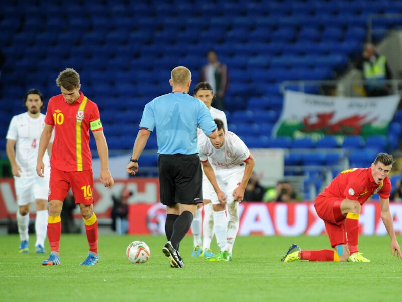 Gareth Bale (rechts) in het shirt van Wales komt overeind na een harde tackle.