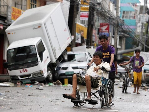 Een Filipijnse man in rolstoel wordt voortgeduwd door de straten van de verwoeste stad Tacloban op de Filipijnen.