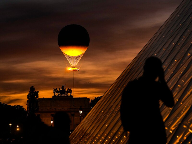 Een man maakt een foto van de piramide bij het Louvre met op de achtergrond de olympische vlam die opstijgt vanuit de Tuilerieën.
