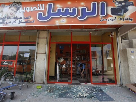Een winkelier in Bagdad veegt glasscherven op, nadat de winkelruit bij de bomaanslag is gesneuveld.