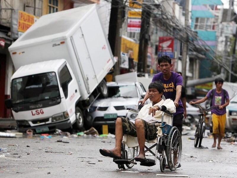 Een Filipijnse man in rolstoel wordt voortgeduwd door de straten van de verwoeste stad Tacloban op de Filipijnen.