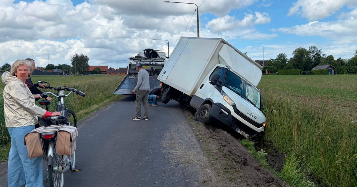 Kleine vrachtwagen sukkelt in gracht tussen de velden in Heule