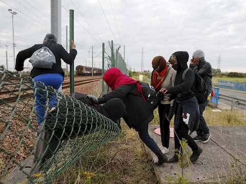 Vluchtelingen klimmen in Calais over een hek om de spoortunnel van de Kanaaltunnel te bereiken.
