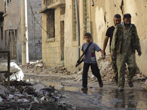 Een kind draagt een kalasjnikov in Syrië.
