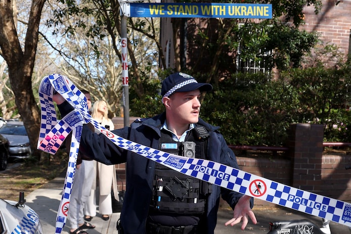Een politieagent haalt de tape bij het Russische consulaat in Sydney weg, zodat de auto die het hek ramde, weggesleept kan worden.