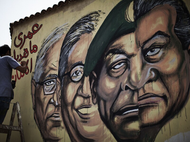 Een graffitikunstenaar schrijft in het Arabisch "Ik zal je nooit vrede wensen" naast de afbeeldingen van oud-president Moebarak (R), legerleider Hussein Tantawi en de presidentskandidaten Amr Mussa (midden) en Ahmed Shafiq (L).