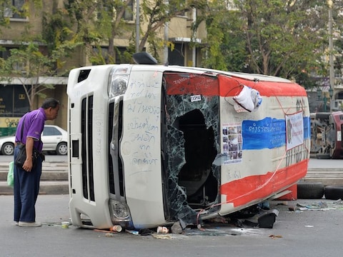 Een man bekijkt een door betogers omver geworpen busje in Bangkok.
