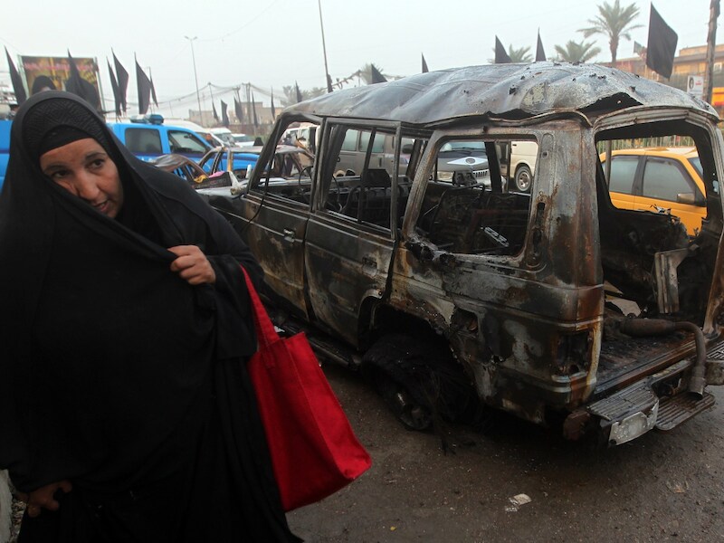 Een vrouw wandelt voorbij het wrak van een bomauto in Bagdad eind november.
