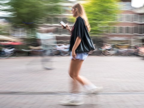 Een meisje loopt met haar telefoon in de hand over een plein.