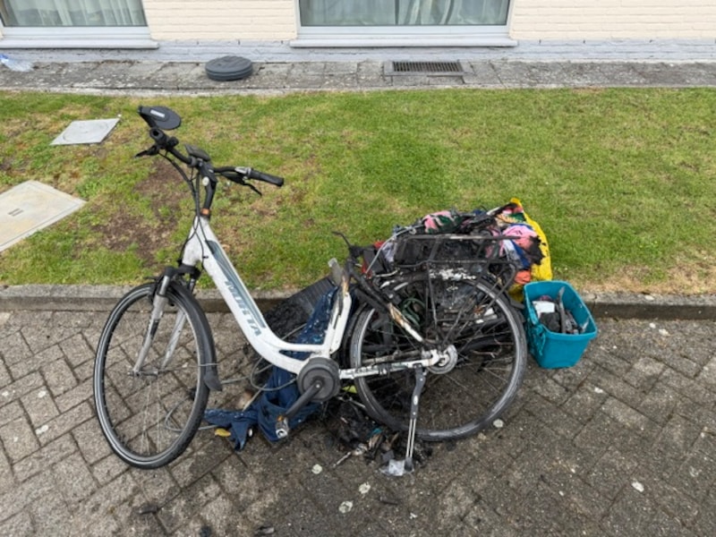 De elektrische fiets liep zware schade op door de intense hitte, waarbij vooral de achterzijde en de batterij volledig wegsmolten en zwartgeblakerd achterbleven op de oprit.