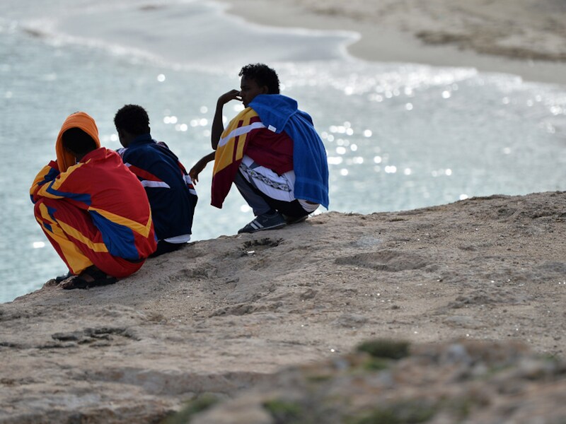 Overlevenden van de ramp zitten op een strand van Lampedusa