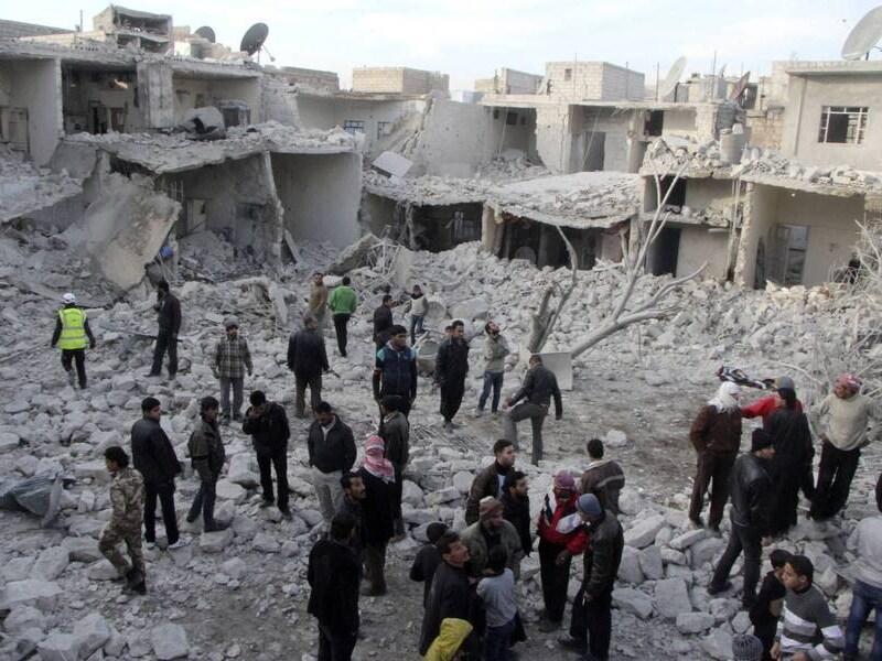 Mensen lopen tussen de brokstukken van vanuit de lucht gebombardeerde huizenblokken in Aleppo.