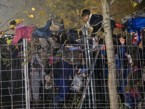 Vluchtelingen helpen kinderen over het hek heen bij Sentilj.